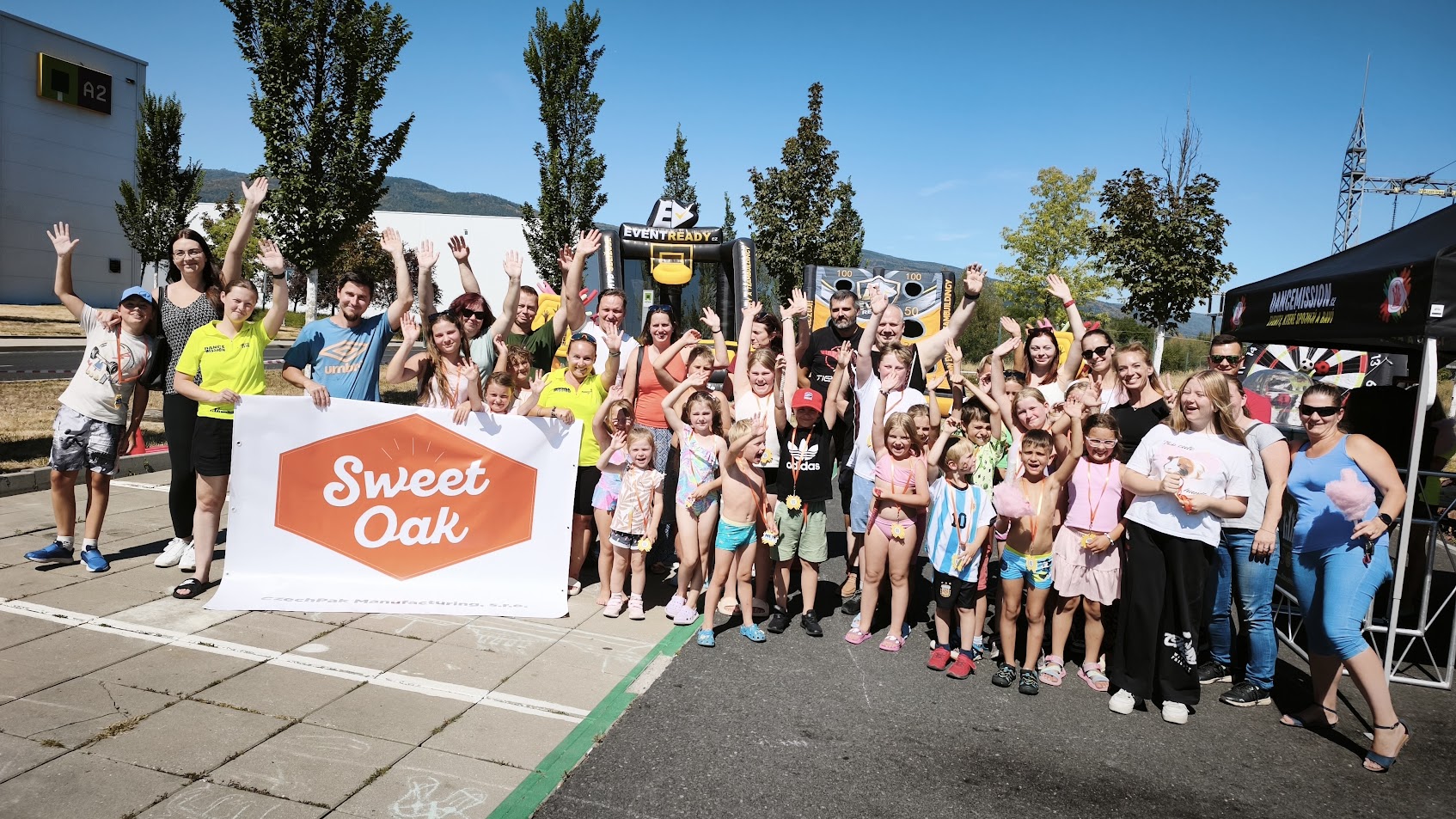 Skupinová fotka dětí a rodičů s bannerem Sweet Oak na firemním táboře