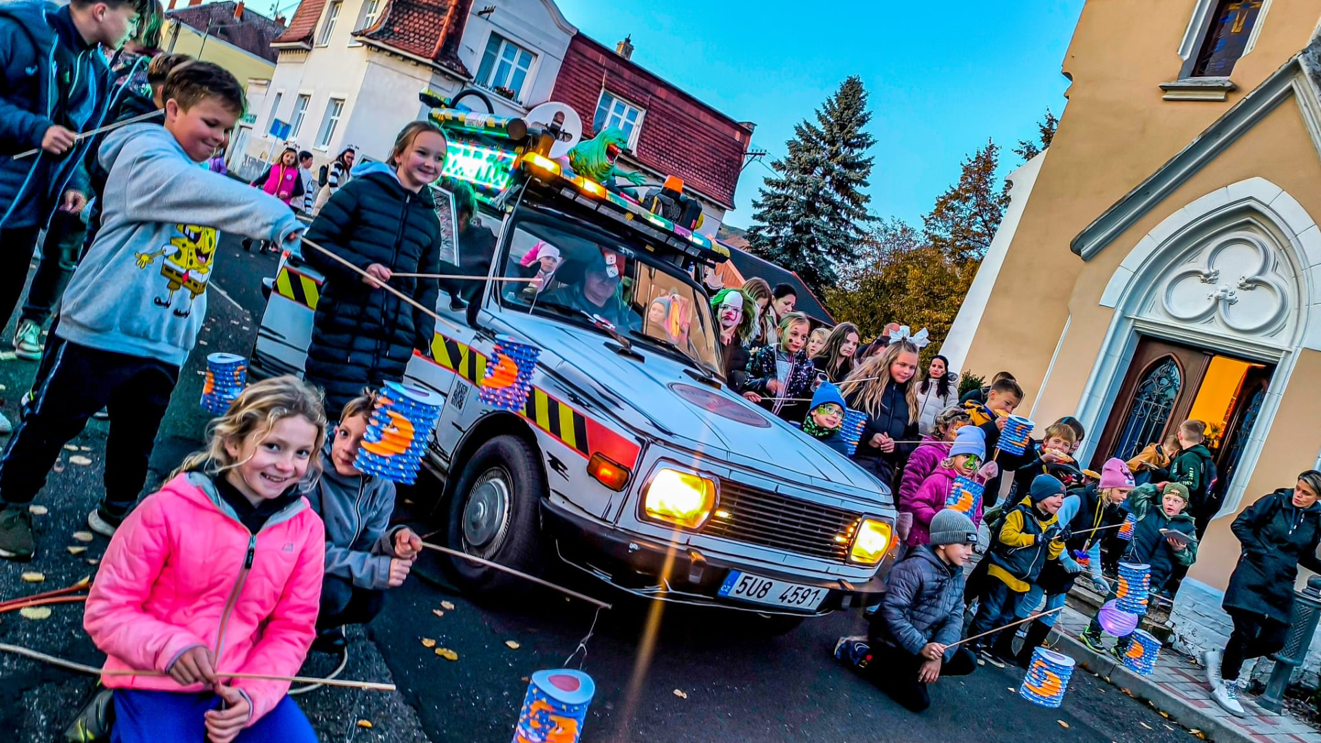 Alegorický vůz Krotitelů strašidel s majáky, slizounem na kapotě a davem dětí s lampiony