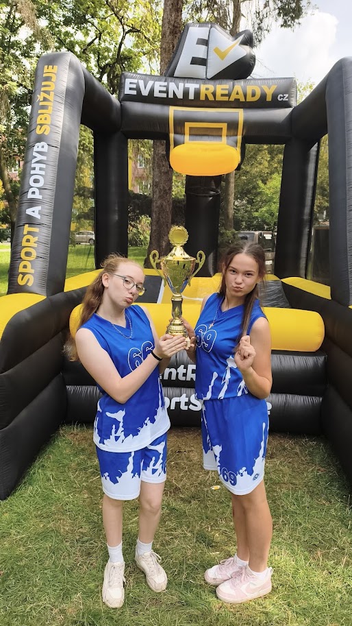 Dvě animátorky v basketbalových dresech se zlatou trofejí u nafukovacího basketu